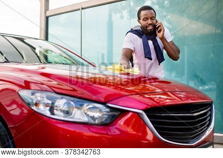 Car Celaning And Polishing Outdoors. Portrait Of Young African Man Cleaning His Car With A Cloth Out
