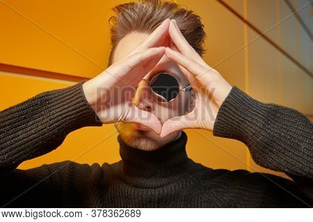 Urban style. Portrait of a stylish young man in black pullover and round mirror sunglasses posing on a street by the yellow industrial wall. Male fashion.