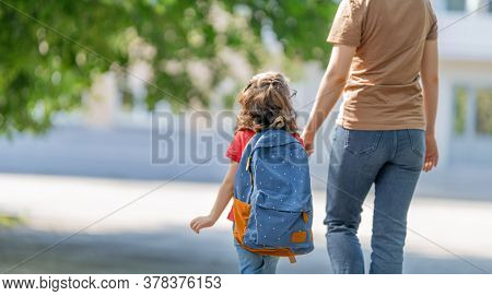 Parent and pupil of primary school go hand in hand. Woman and girl with backpack behind the back. Beginning of lessons. First day of fall.