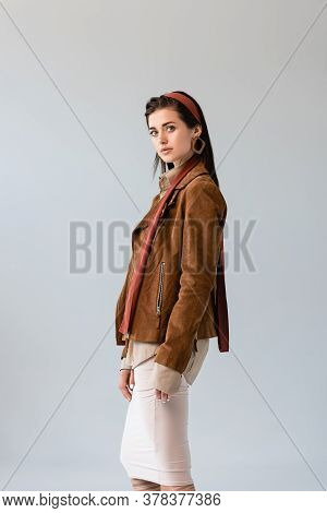 Attractive, Fashionable Girl In Suede Jacket Looking At Camera Isolated On Grey