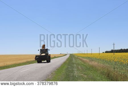 Tractor After Harvest On The Road On A Sunny Summer Day. Copy Space.