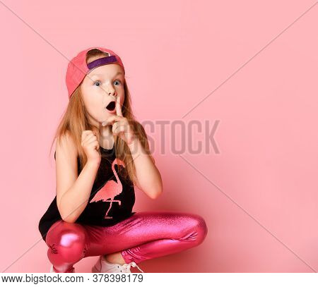 Sly Little Girl Hunkering Down And Holding Her Index Finger Close To Opened Mouth Begging To Save A 