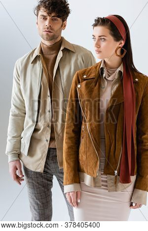 Fashionable Man Looking At Camera Near Attractive Girl In Stylish Suede Jacket Isolated On Grey