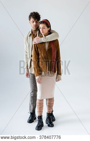 Full Length View Of Stylish Man Embracing Trendy Woman In Suede Jacket Isolated On Grey