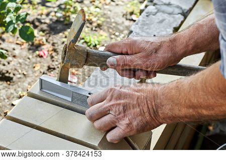 Bricklayer Installing Bricks On The New Fence From Facing Bricks Using Hammer And Building Level.