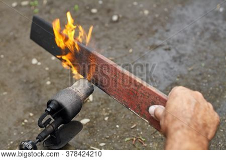 A Man Is Burning The Board Using The Old Rusty Blowtorch. Handmaking Manufacturing Process Of Burnt 