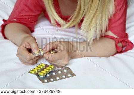 Woman With Pills, Female Hands On A Bed With A Blister Pack Of Tablets. Blonde Girl Taking Medicatio