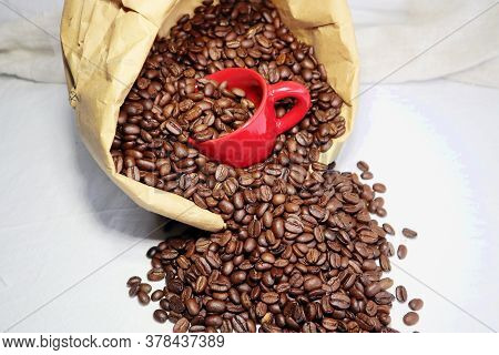 Red Ceramic Cup Full Of Coffee Beans In A Paper Bag On A Table