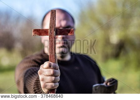 A Man Holds A Wooden Christian Cross In Front Of Him, An Ax In His Other Hand. The Concept Of Castin