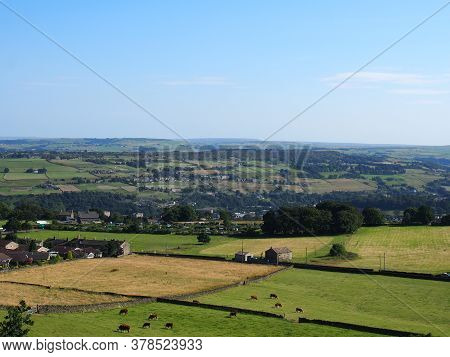 View Of The Village Of Luddenden In The Calder Valley Surrounded By Trees And Cows Grazing In Fields