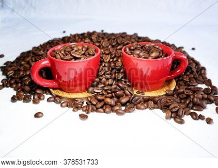 Red Ceramic Cups And Lot Of Coffee Beans On A White Table