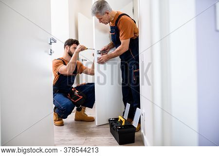 Full Length Shot Of Two Locksmith, Repairmen, Workers In Uniform Installing, Working With House Door