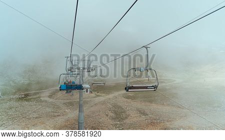 Cableway Near Smoke In Rocky Countryside. Modern Ropeway Located On Stony Ground Near Thick Fume In 