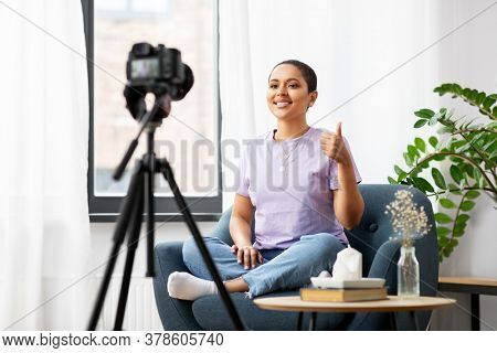 blogging, videoblog and people concept - happy smiling african american female video blogger with camera videoblogging at home and showing thumbs up
