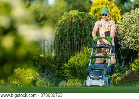 Beautiful Garden Backyard Grass Mowing By Caucasian Men In His 40s. Gardener And His Modern Mowing E