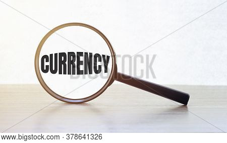 Magnifying Glass With Text Currency On Wooden Table.