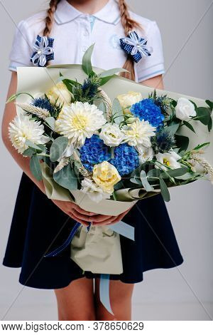 A Bouquet Of Flowers, Packed In Beige Paper In The Hands Of A Girl With Pigtails On A Light Backgrou