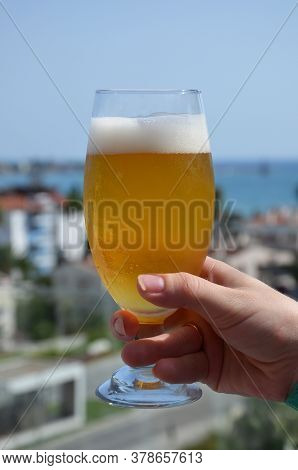 Hand Holding A Glass Of Beer In Beach Tropical Sea Background. Vacation Holiday Concept