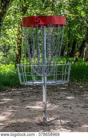 A Red #5 Disc Golf Basket Empty In The Woodlands On A Course In The Park In The Shade On A Sunny Day