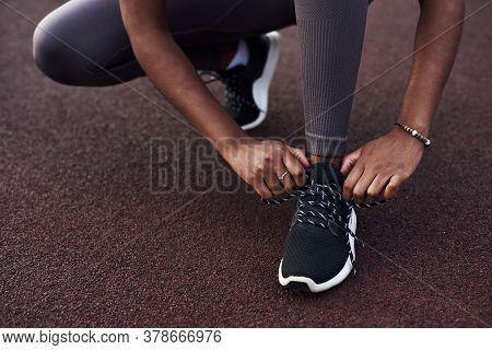 Black Girl Laces Up Her Sneakers While Doing Sports On The Street. Outdoor Fitness Concept.
