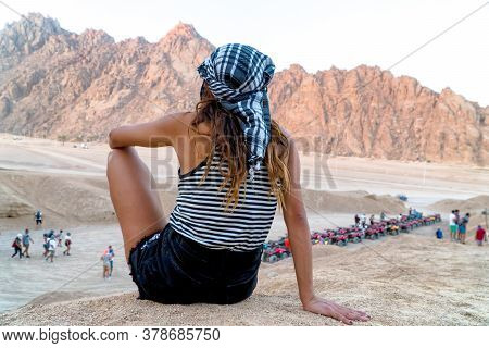 A Beautiful Girl In Black Shorts And Kefiah Admires Particular Egyptian Red Hills.