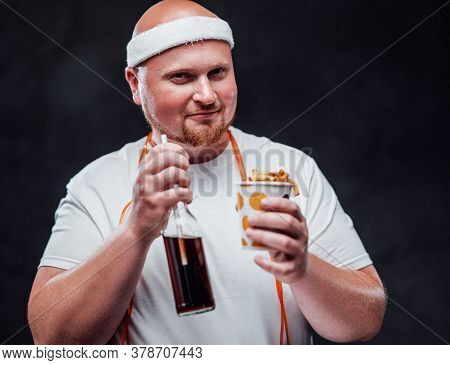 Pleased Chubby Man In A White Duffle, Eating French Fries With Sauce And Drinking Sweet Coca Cola