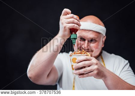 Plump Bald Man In A White Duffle And With A Headband On His Head, Eating French Fries With Sauce Wit