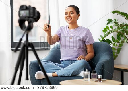 blogging, videoblog and people concept - happy smiling african american female beauty blogger with camera and make up cosmetics videoblogging at home