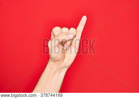 Hand of caucasian young man showing fingers over isolated red background showing little finger as pinky promise commitment, number one