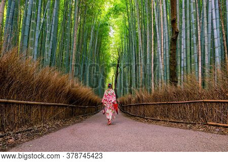 Woman In Traditional Yukata With Red Umbrella At Bamboo Forest Of Arashiyama In Kyoto, Japan