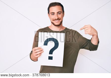 Young handsome man holding question mark pointing finger to one self smiling happy and proud 