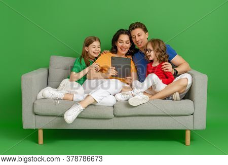 Happy loving family on bright color background. Father, mother and daughters girls using tablet pc for remote conversation with friends. Dad, mom and lovely children are having fun staying at home.