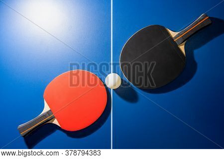 Top View Black And Red Table Tennis Racket And A White Ping Pong Ball On The Blue Ping Pong Table Wi