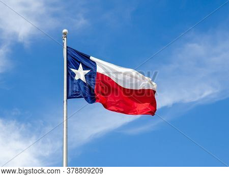 Texas State Flag On The Pole Waving In The Wing Against Blue Sky And White Clouds