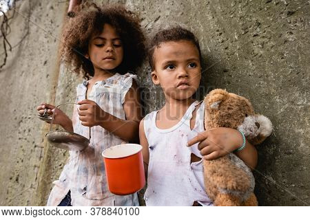 Selective Focus Of Poor African American Boy Holding Dirty Teddy Bear While Begging Alms Near Sister