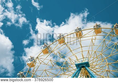 Ferris Wheel Against The Background Of The Cloudy Sky. Yellow And Blue Shades. Empty Attraction. Cop