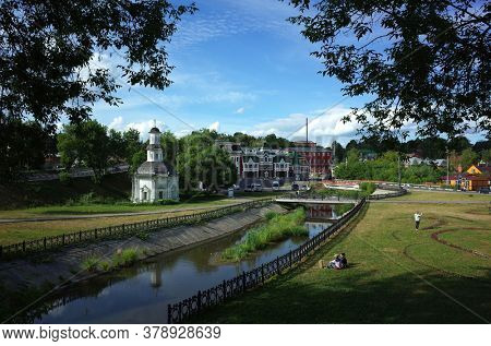 Sergiyev Posad, Russia - June 25, 2019: People sitting on the bank of Konchura river with view of white Chapel of the Pyatnitsky well