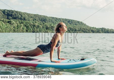 Middle Age Caucasian Woman Practising Yoga On Paddle Sup Surfboard At Sunset. Female Stretching Doin