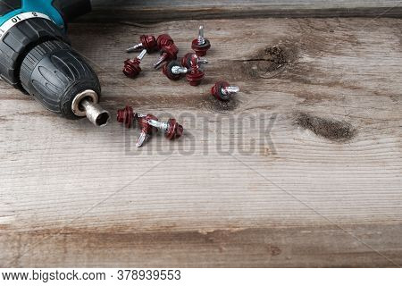 Cordless Drill Screwdriver And Self-tapping Screws For Metal On An Old Wooden Background With A Plac