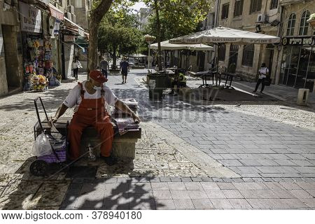 Jerusalem, Israel - July 30th, 2020: A newspaper man and a street cleaner sitting idly on Ben - Yehuda pedestrian mall, usually a crowded main street of Jerusalem, almost empty at COVID times.
