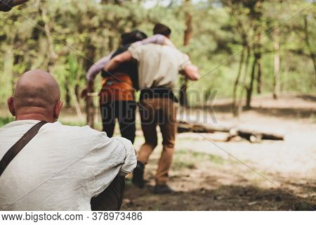 Two Men From The Back In Nature. A Bald Man From The Back Is Watching Them. A Friend Helps A Friend 