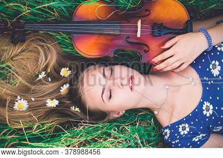 Young Slim Fair-skinned Girl Blonde Beautiful Lies In Tall Grass. A Woman Hugs Violin.