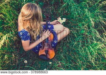 Woman Sit In Tall Grass And Hugs Violin