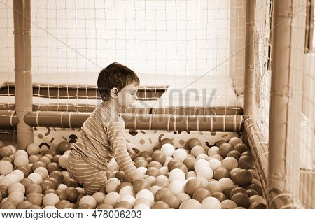 Toddler Baby Plays In The Pool With Balls. Child Boy Crawling In The Pool With Plastic Balls. Kid Ag