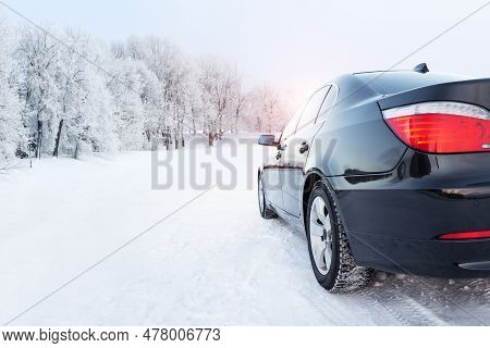 Black Car On A Winter Road In A Snowy Forest, Winter Journey. Modern Car With Winter Tires On Snowy 