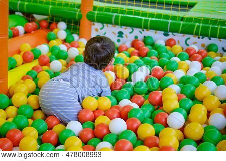 Toddler Baby Plays In The Pool With Balls. Child Boy Crawling In The Pool With Plastic Balls. Kid Ag