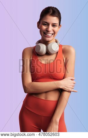 Positive Young Female Athlete In Orange Top And Bra With Wireless Headphones Smiling And Looking At 