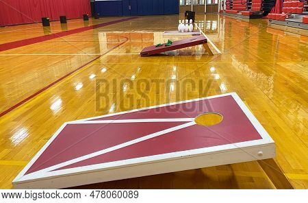 Side View Of Homeade Cornhole Game Boards And Bowling Set Up In A Gymnasium For Gym Class.