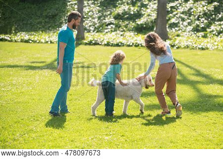 Mother, Father And Son Are Running With Dog In Park. Happy Young Family Spending Time Together Outsi