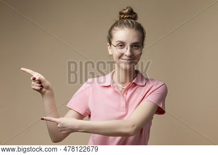 Caucasian Blond Female Girl In Round Glasses Wearing Tshirt And Showing Direction Against Beige. Hor